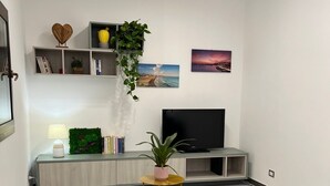 Una sala de estar moderna con un televisor de pantalla plana grande, un sofá, una mesita auxiliar y una estantería con adornos.