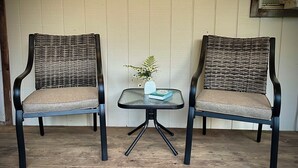 Twee rieten stoelen met comfortabele zittingen en rugleuningen, geplaatst op een houten vloer met een kleine glazen tafel ertussen.