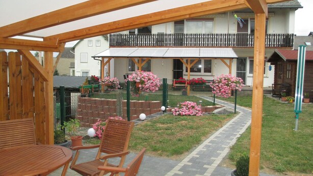 A wooden pergola with a brick pathway leading to a seating area with wooden furniture. - Vacation apartments Hehner attic (Patersberg)