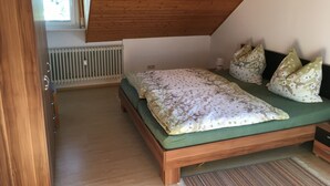A bedroom with a wooden ceiling, a green bed with floral bedding, and a radiator. - Vacation apartments Hehner attic (Patersberg)