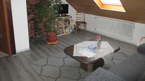 A cozy attic room with a skylight, a potted plant, a bookshelf, and a table with a vase. - Vacation apartments Hehner attic (Patersberg)
