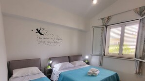 A hotel room with two beds, a wall decoration, and a window with blinds. - Vacation home "Fortuna " (Balestrate)