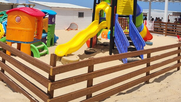 A beach play area with a wooden fence, a yellow slide, and various colorful play structures. - Vacation home "Fortuna " (Balestrate)