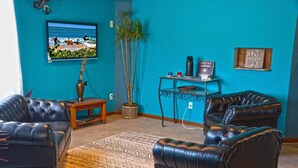 Una sala de estar con una pared color turquesa, un televisor, una mesa de centro, dos sofás de cuero, una alfombra estampada y una planta en maceta.