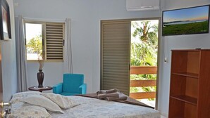 Un dormitorio con una cama, una silla azul, un armario de madera y un televisor en la pared.