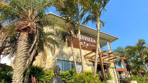 Un hotel con un letrero que dice "HERRUGEM Suites", rodeado de palmeras y una estatua de Buda.