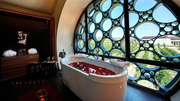Un baño moderno con una bañera grande, un tocador de madera y un diseño de ventana circular único.