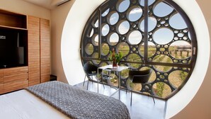 Un dormitorio con un ventanal circular grande, una cama, un televisor y una pequeña mesa con sillas.