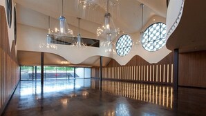 Un interior espacioso con diseño moderno, que presenta una amplia área abierta con piso reflectante, una estructura de techo original y grandes ventanales circulares.