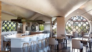 Una cocina moderna con una isla central, asientos tipo barra y un comedor con mesas y sillas redondas.