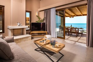 A modern living room with a sofa, a TV, a wooden coffee table, and a balcony with a view of the sea. - Terra Lucis Mountain Residences/ Aether Villa (Agios Leon)