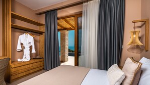 A hotel room with a bed, a wooden dresser, a robe hanging on the wall, and a view of the sea through a glass door.