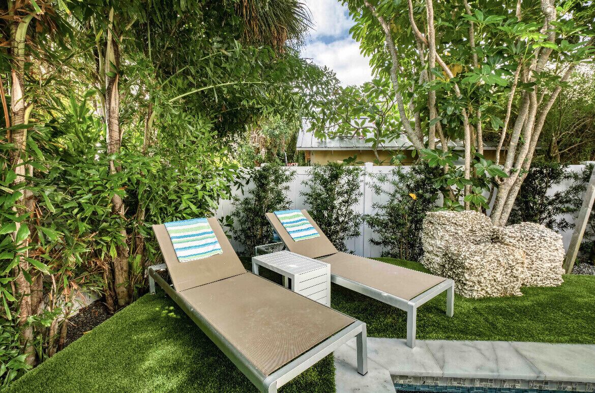 A backyard with two lounge chairs, a small table, and a rock feature.