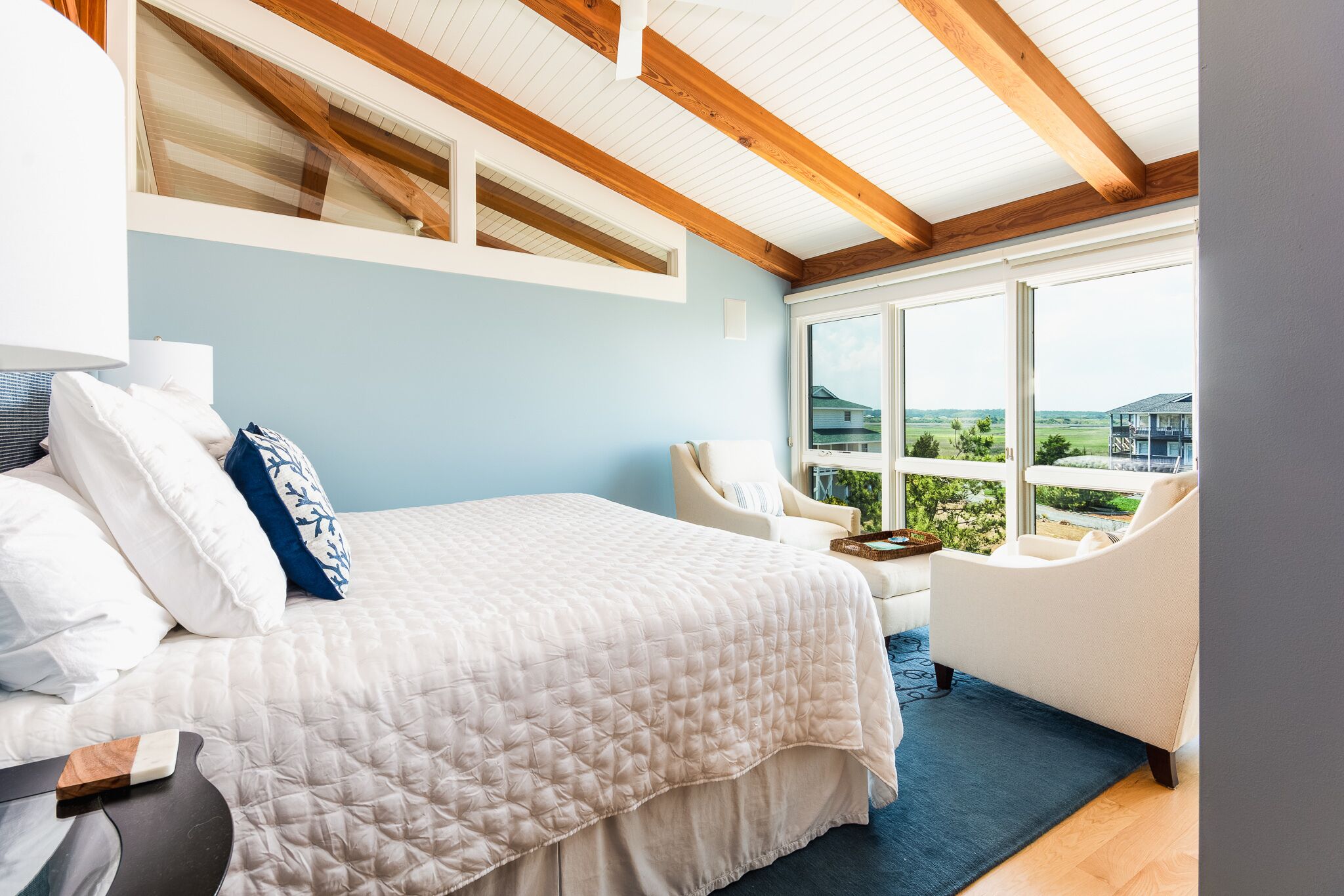 Une chambre à coucher avec un lit, deux chaises, une fenêtre donnant sur un beau paysage et des poutres en bois au plafond.