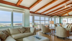 A spacious living room with a large window overlooking the beach, a wooden ceiling, and a cozy seating area. - "Aqualuxe" Luxury oceanfront 6 bedroom, 5.5 bathroom home with New Pool for 2022 Season (Holden Beach)