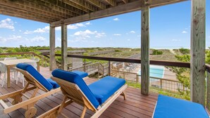 A wooden deck with two lounge chairs and a table, overlooking a beach and a pool. - "Aqualuxe" Luxury oceanfront 6 bedroom, 5.5 bathroom home with New Pool for 2022 Season (Holden Beach)