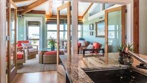 A spacious living area with a large window, a kitchen with granite countertops, and a dining area with wicker furniture. - "Aqualuxe" Luxury oceanfront 6 bedroom, 5.5 bathroom home with New Pool for 2022 Season (Holden Beach)