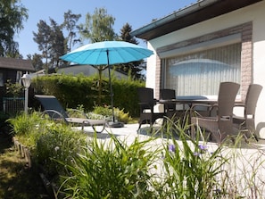 Une terrasse extérieure avec une table et des chaises, un parasol bleu et un fauteuil de relaxation.