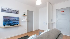 Un soggiorno moderno con una TV a schermo piatto, un divano, un tappeto piccolo e una porta con la scritta 'EMERGENCIA 112'.