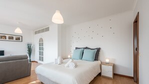 A modern bedroom with a large bed, bedside tables, a grey sofa, and a wall-mounted light fixture. - GuestReady - Porto Magic View (Vila Nova de Gaia)