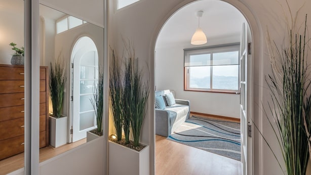 A modern interior with a hallway leading to a living area, featuring a sofa, a large window, and decorative plants. - GuestReady - Porto Magic View (Vila Nova de Gaia)
