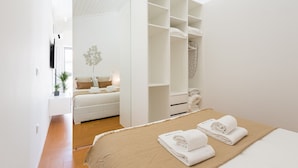 Une chambre moderne avec un grand lit, un dressing et un petit coin salon agrémenté d’une plante.