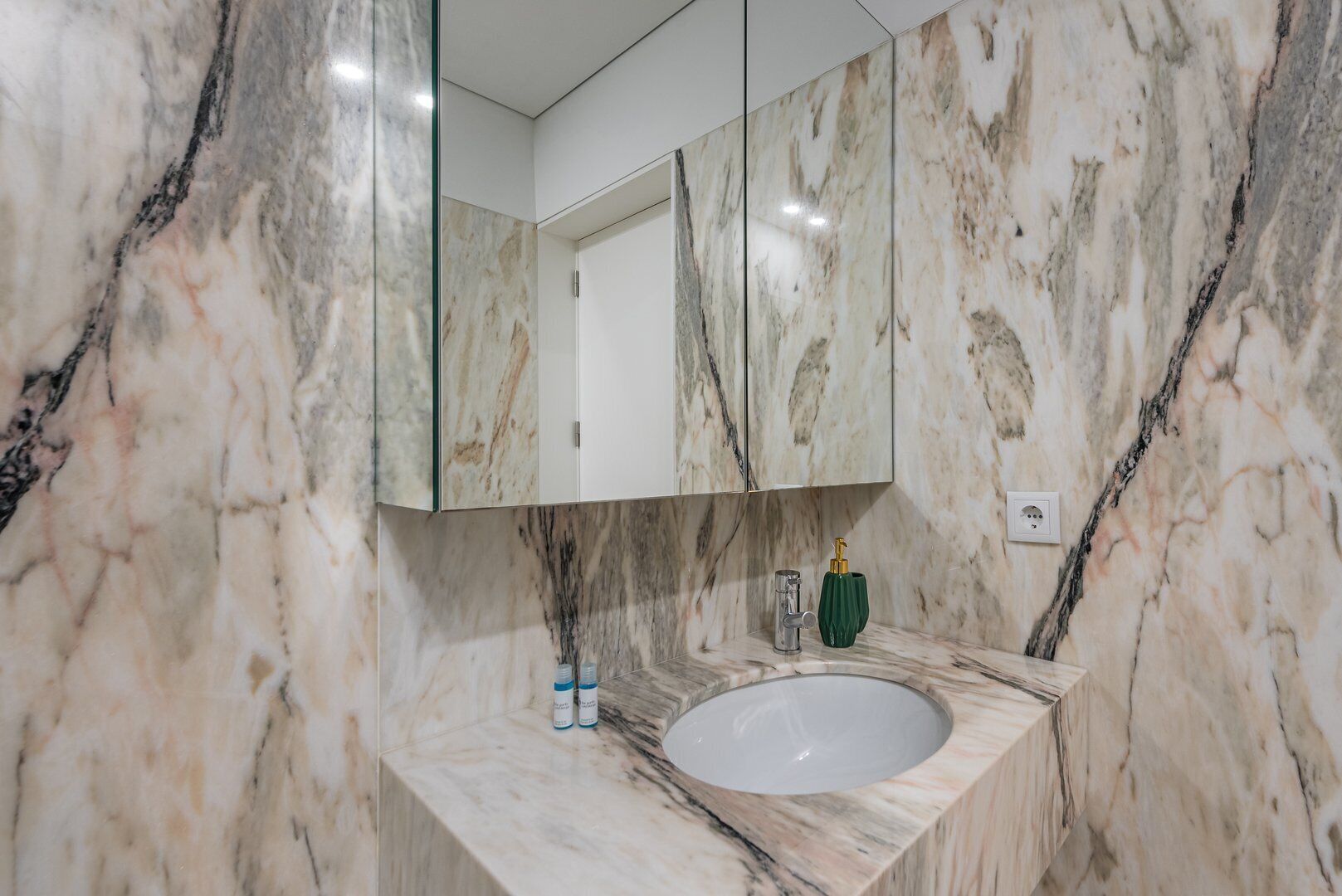 A bathroom with a marble sink, a mirror, and a green soap dispenser.