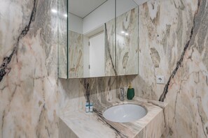 Une salle de bain avec un lavabo en marbre, un miroir et un distributeur de savon vert.