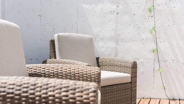 Poltrone da lounge in vimini con cuscini, appoggiate a un muro bianco con superficie strutturata.