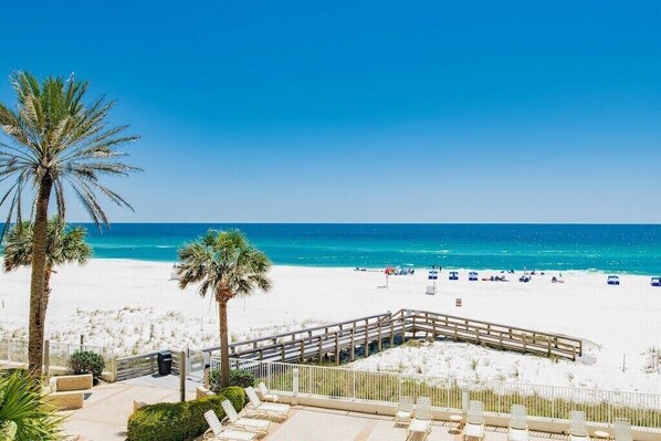 A beach view with a wooden deck, palm trees, and beach chairs.