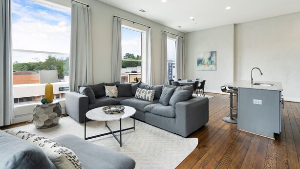 Una sala moderna con un sofá gris, una mesita de centro redonda y una cocina con encimera y fregadero grises.