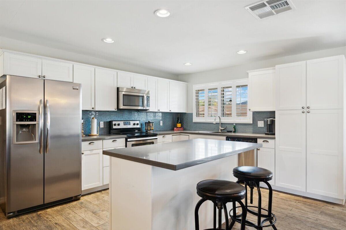 A modern kitchen with white cabinets, stainless steel appliances, and a central island with stools.