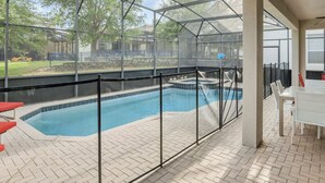 A covered outdoor swimming pool with a glass enclosure, a patio area with a table and chairs, and a view of the surrounding landscape.