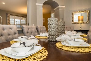 A dining area with a long table set for a meal, featuring grey upholstered chairs, white plates, and a decorative vase. - A Disney Themed Home, Just Minutes From CDC Standards! #rwh7728 (Kissimmee)
