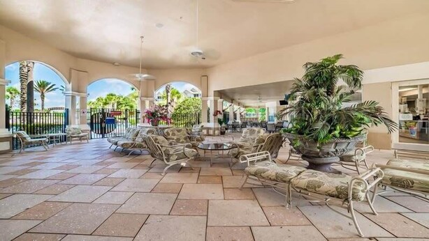 A spacious indoor area with a central seating area, surrounded by potted plants and a view of the outdoors.