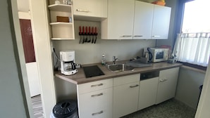 A compact kitchen with white cabinets, a coffee maker, a microwave, and a sink.