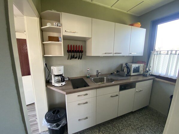 A compact kitchen with white cabinets, a coffee maker, a microwave, and a sink.