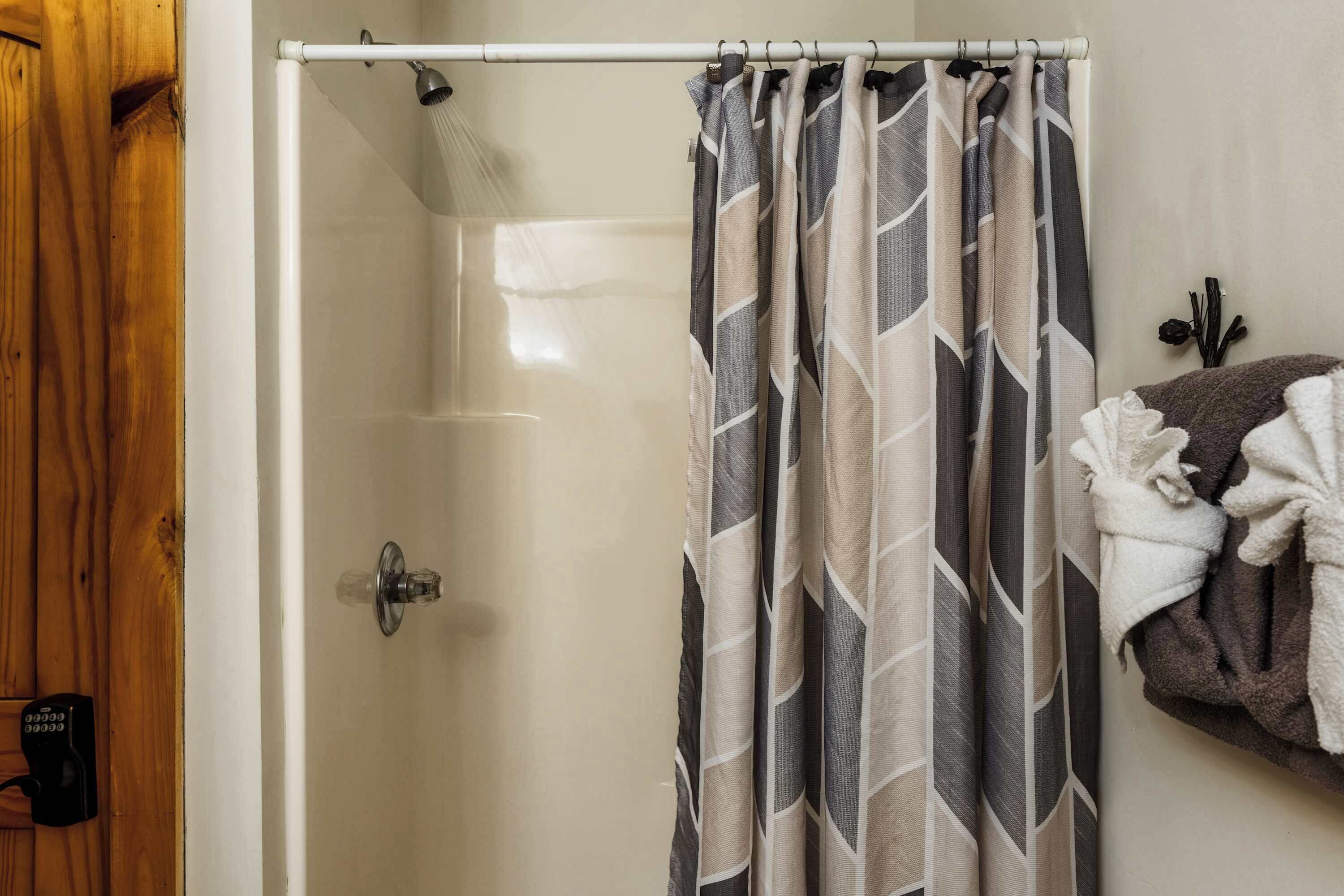 A shower area with a patterned shower curtain, a towel rack with towels, and a wooden door.