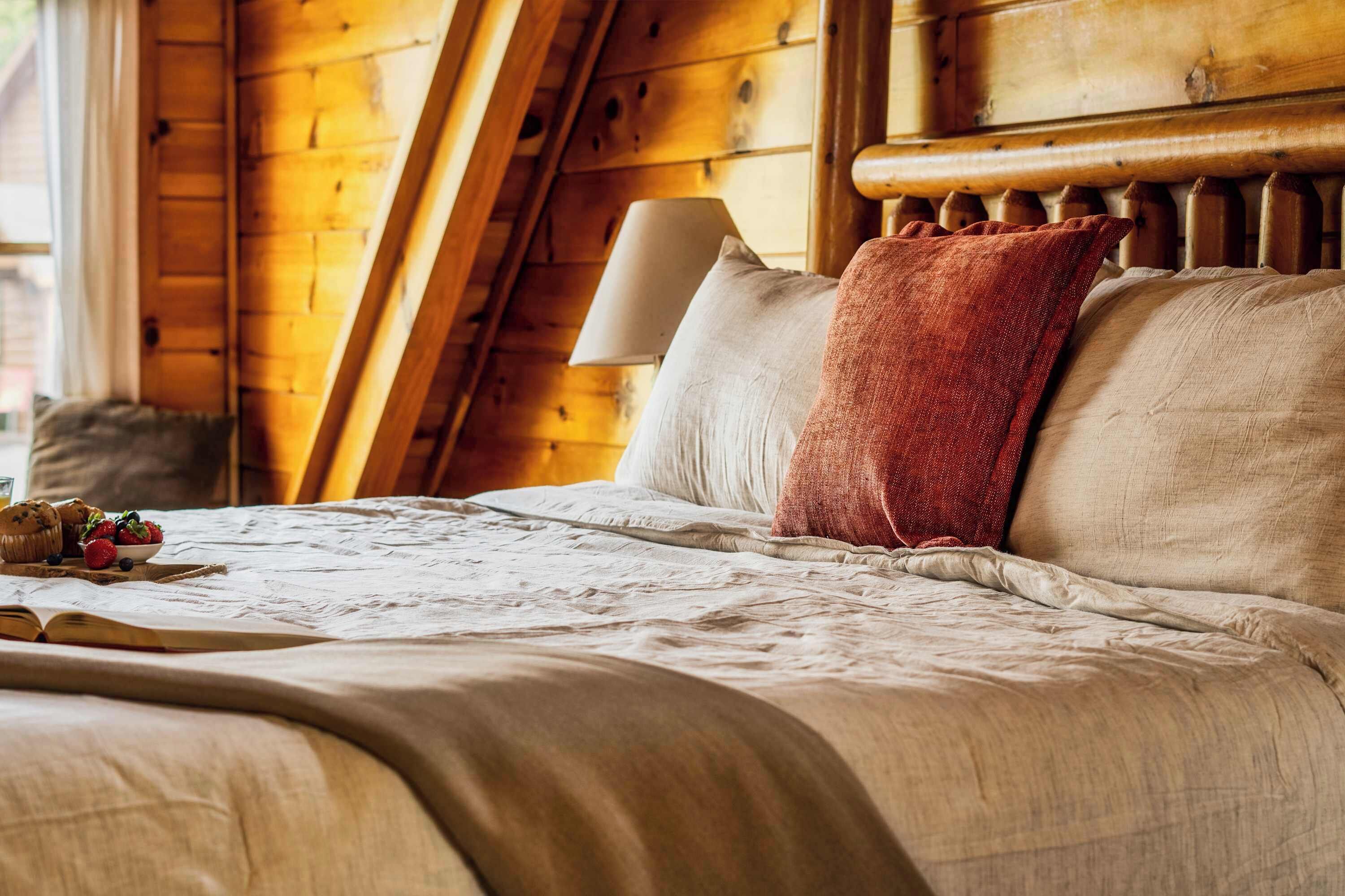 A cozy wooden room with a bed, pillows, and a lamp.