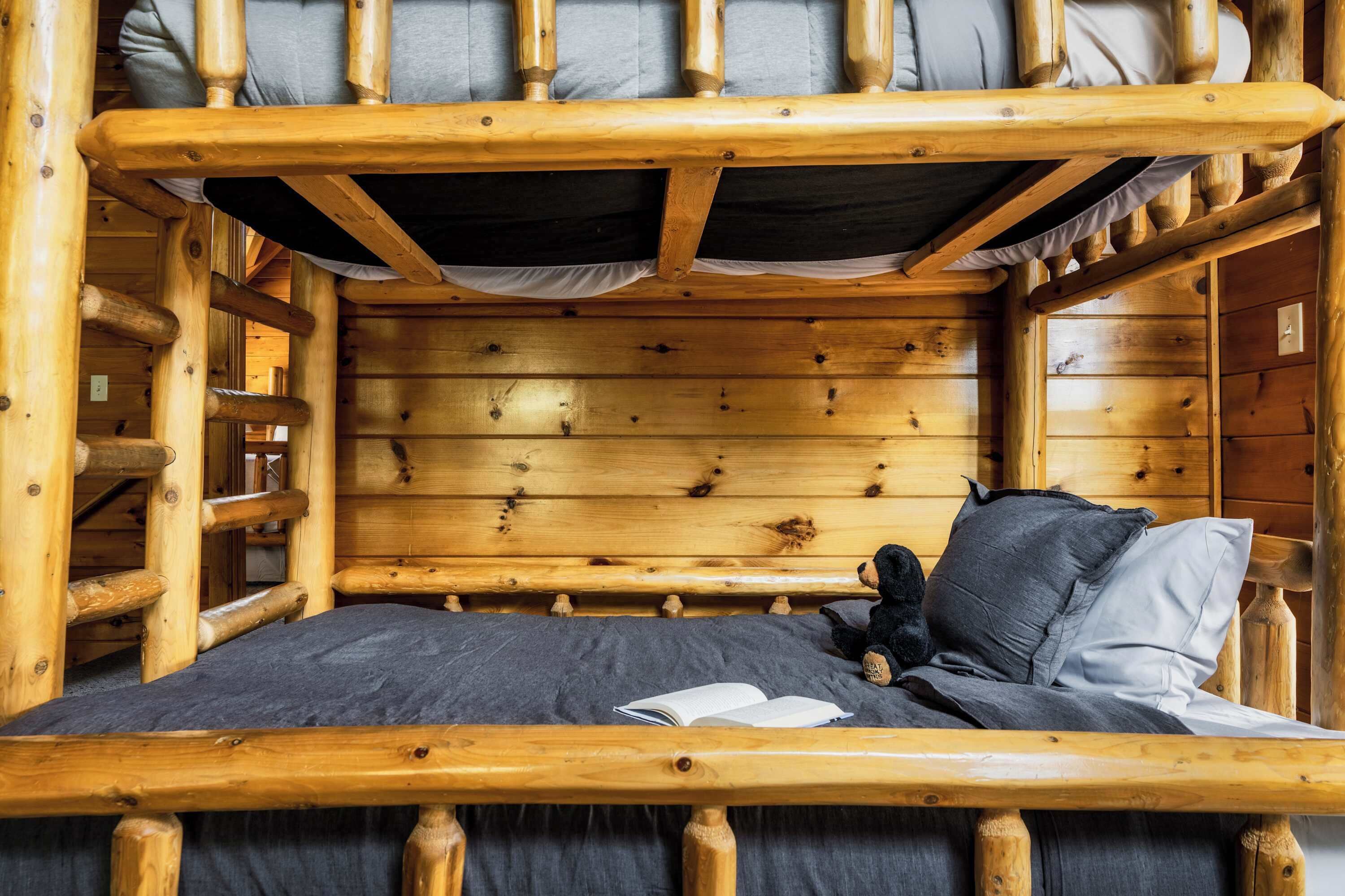 Una cama litera de madera con colchón y almohadas, un libro sobre la cama y un osito de peluche.
