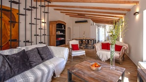 A spacious living room with a high ceiling, wooden beams, a sofa, chairs, a table with a vase and fruit bowl, and a bookshelf. - Charming house -A STALLA- Between Sea and Mountain (Muro Hute Corse)