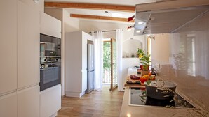 A modern kitchen with white cabinetry, a built-in oven, and a stove. There is a window with curtains, a plant on the counter, and a view of the outdoors. - Charming house -A STALLA- Between Sea and Mountain (Muro Hute Corse)