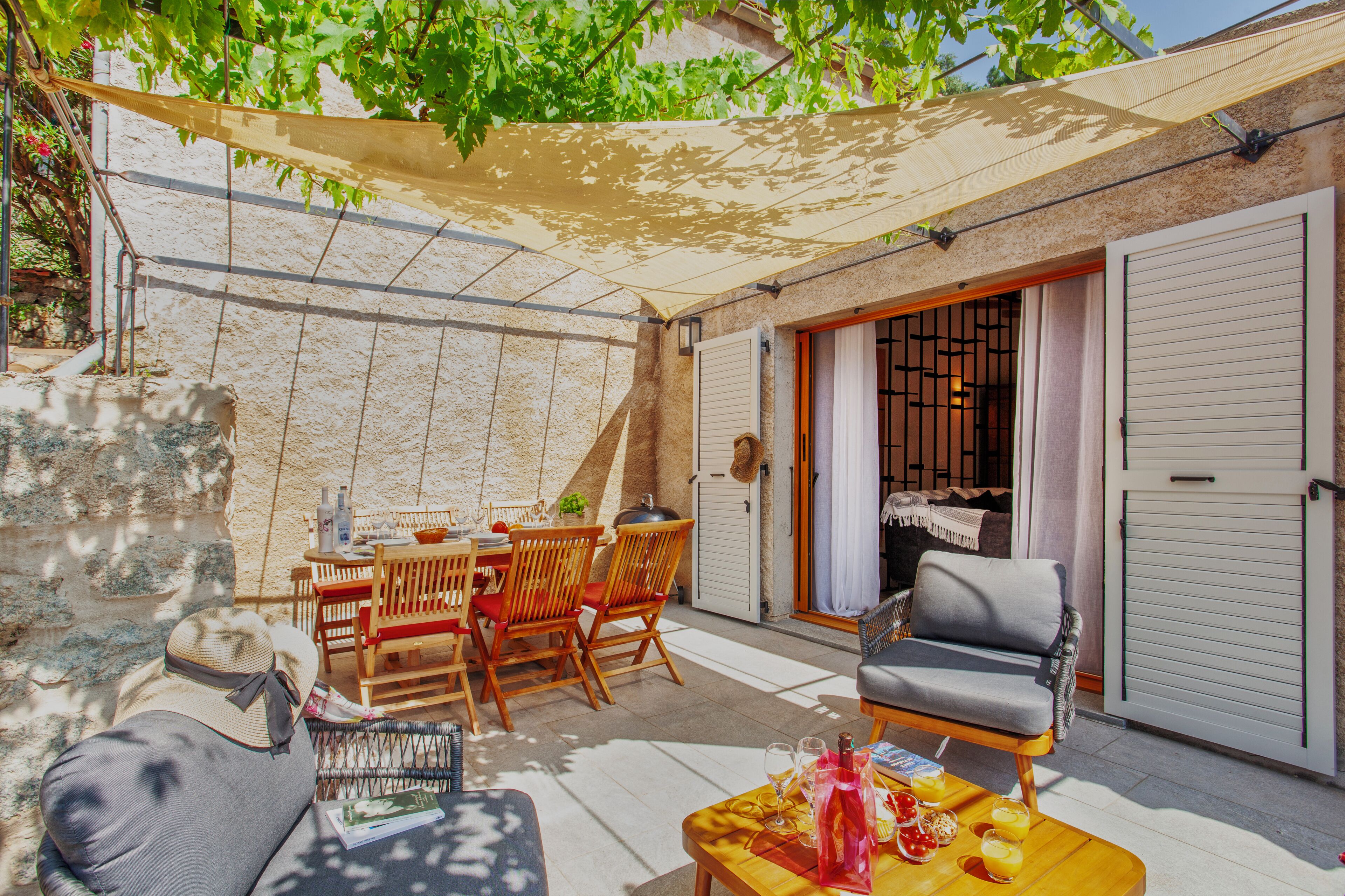 A patio area with a table, chairs, and a sofa. There is a sliding door and a covered seating area.