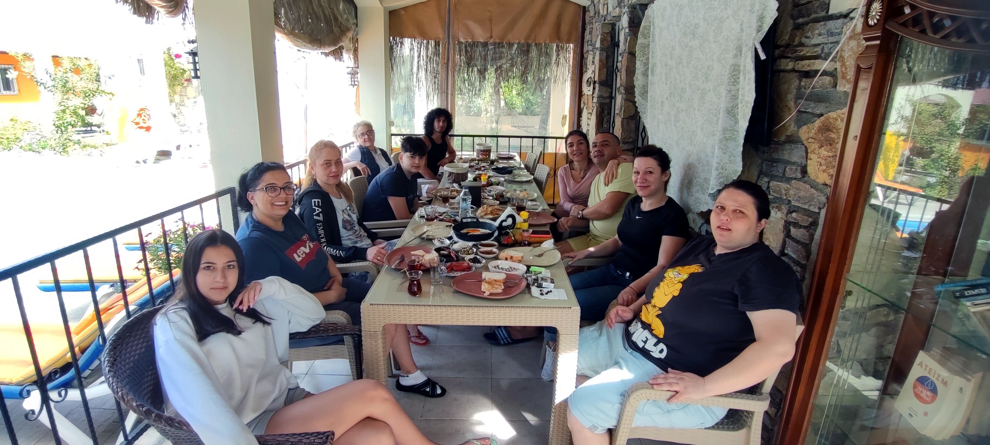 A group of people seated around a table on a patio with a stone wall and a glass door.