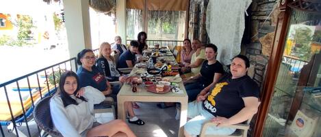 A group of people seated around a table on a patio with a stone wall and a glass door.
