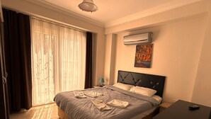 A hotel room with a bed, a bedside table, an air conditioner, a painting, and a window with curtains. - Cileks Apart Otel (Fethiye)