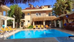 A pool area with lounge chairs and a bar area with a flag. - Cileks Apart Otel (Fethiye)