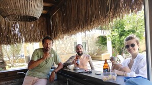 A group of people sitting at an outdoor table with a stone wall and greenery in the background. - Cileks Apart Otel (Fethiye)