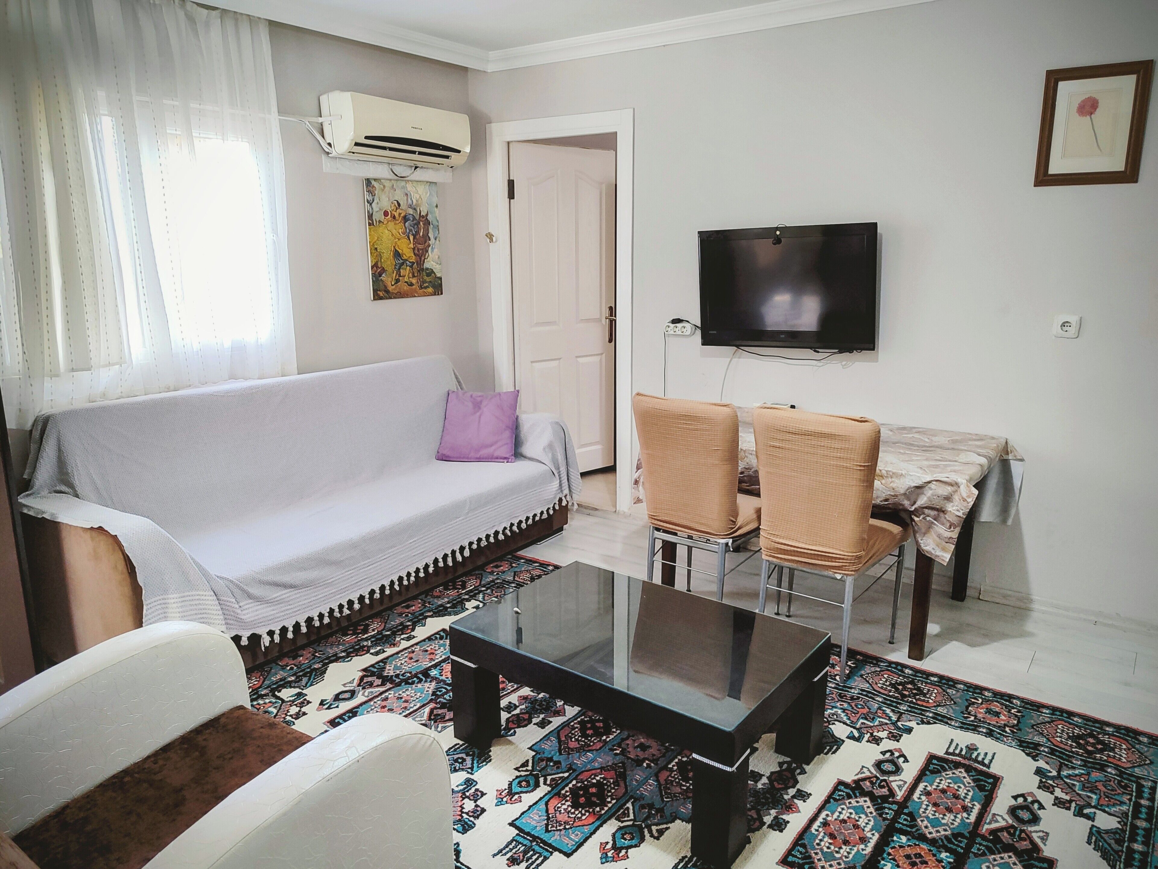 Un salon comprenant un canapé, deux fauteuils, une table basse, un téléviseur et un tapis à motifs.