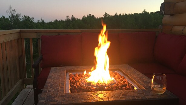 Feuerstelle mit Steinkonstruktion auf einer Holzterrasse, ausgestattet mit roten Kissen.